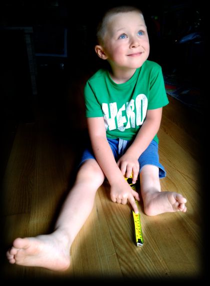 Mały chłopiec w zielonej koszulce, siedzi na podłodze, patrzy w górę, jedną nóżkę ma wyraźnie krótszą.